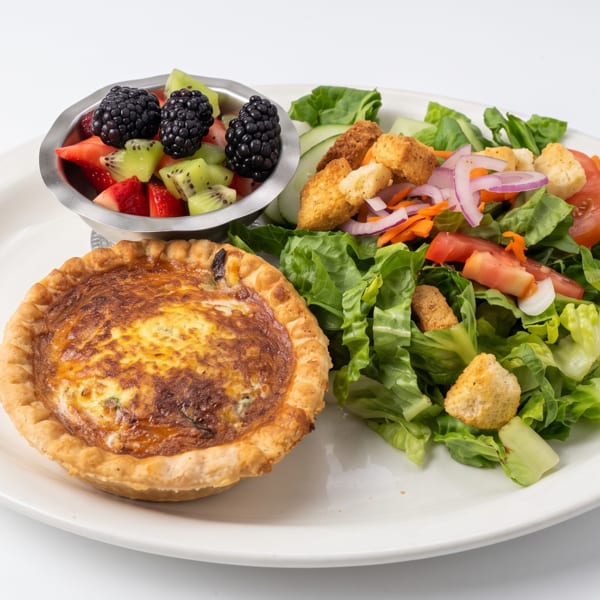 Individual quiche, mixed green salad, and a fruit cup with blackberries, kiwi, and strawberries.