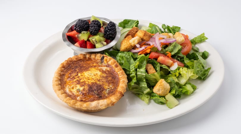 Individual quiche, mixed green salad, and a fruit cup with blackberries, kiwi, and strawberries.