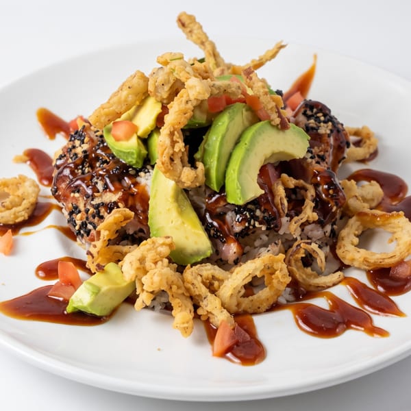 Sesame-crusted tuna bowl with rice, avocado, diced tomatoes, crispy fried onions, and a dark glaze.