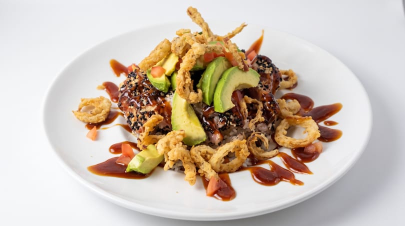 Sesame-crusted tuna bowl with rice, avocado, diced tomatoes, crispy fried onions, and a dark glaze.