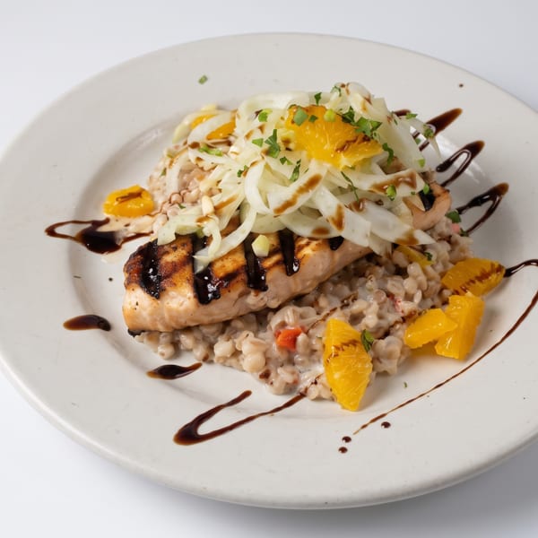 Grilled salmon fillet with fennel, orange segments, and balsamic glaze on a bed of farro.
