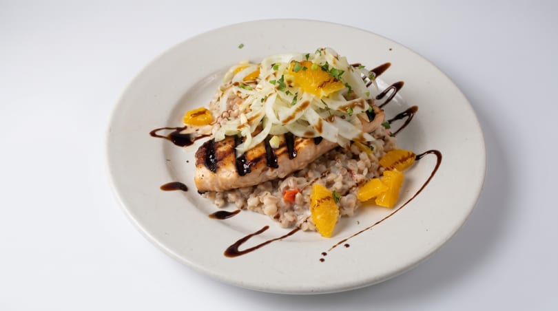 Grilled salmon fillet with fennel, orange segments, and balsamic glaze on a bed of farro.